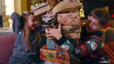 Oturma odasında oynayan neşeli ve neşeli kardeşlerimiz evde eğlenerek Noel hediyeleri kulesi yapıyorlar. Madalyalı Noel ağacı. Kış zamanı. Aileler.