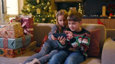 Noel ailesi. Noel ağacının altındaki kanepede oturmuş video oyunları oynayan iki sevimli beyaz kardeş. Kış tatili Tasasız çocukluk.
