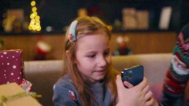 Akıllı telefon uygulaması kullanarak kanepeye oturmuş Noel süslemeli ağacın yanında video oyunları oynayan iki komik çocuk. Kış tatili.