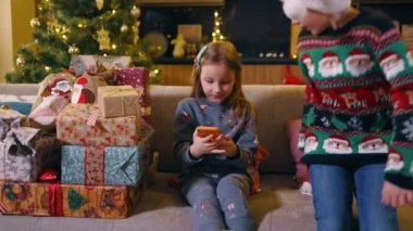 Noel arifesinden önce oynayan birkaç beyaz çocuk. Xmas şapkalı komik çocuklar akıllı telefon kullanarak eğleniyorlar. Kardeşler..