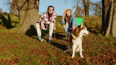 Sonbahar ormanlarında romantik, mutlu, güler yüzlü, sevimli çift evcil köpekle oturuyor. Hayvan gibi rahat, neşeli bir portre. Gün ışığında. Yavaş çekim