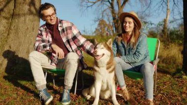 Güz parkında ya da ormanda evcil köpekle oynayan sevimli bir çift. Güçlü. Hayvan gibi rahat, neşeli bir portre. Gülümseyerek mutlu ol. Gün ışığında. Yavaş çekim