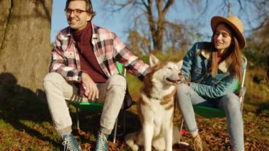 Güz parkında ya da ormanda evcil bir köpekle oynayan genç bir çift portresi. Güçlü. Hayvanlar neşeli. Gün ışığında. Rahatlama zamanı. Yavaş çekim