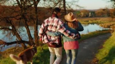 Güz Ormanı 'nda göl kenarında evcil bir köpekle yürürken kadın ve erkeği vurdular. Hayvan gibi rahat, neşeli bir portre. Mutlu ol. Gün ışığında. Yavaş çekim