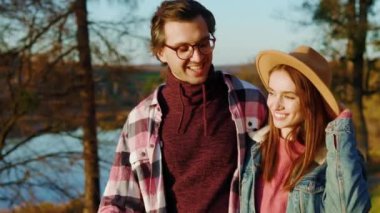 Çekici erkek ve kadın güzel çift göl kenarındaki sonbahar ormanında gülümsüyor. Hayvan gibi rahat, neşeli bir portre. Mutlu ol. Gün ışığında. Yavaş çekim