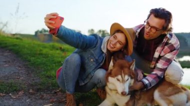 Güz Ormanı 'nda gölün yanında, telefonda köpekli sevimli bir çift selfie çekiyor. Manzaralı tatil ilişkisi hayvanları. Doğa. Yavaş çekim