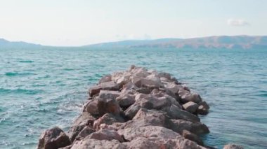 Gri kayalara vuran dalgaların yakın çekim görüntüleri. Hava güzel. Turkuaz Adriyatik denizinin muhteşem manzarası. Arka planda dağlar olan muhteşem bir manzara. Dışarıda, gündüz, dinlenme, yaz tatili.