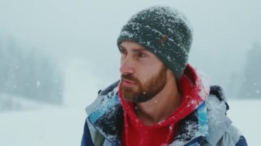 Yeşil örgü şapkalı yakışıklı genç sakallı adamın portresi kar ormanlarında kameraya bakıyor. Çekici bir doğa. Kapatın. Yavaş çekim