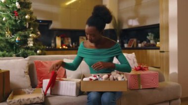 Afro-Amerikan portresi. Kanepede oturan güzel genç bayan. Ve dekore edilmiş odada Noel hediyesi kutusu hazırlıyor. Yeni yıl. Tatil kutlaması. Noel ağacı. Hediye. Yavaş çekim