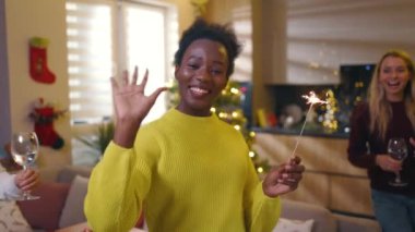 Bir grup çok ırklı arkadaş ellerinde yanan maytaplarla Noel 'de evde kameraya bakıyorlar. Geleneksel tatil. Kutlama. Mutlu noeller. Kış zamanı. Yavaş çekim