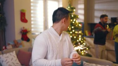 Komik çok ırklı arkadaşlar yılbaşı partisi veriyor yanan maytaplar tutuyor şarap içiyor ve evde kameraya gülümsüyorlar. Geleneksel tatil. Kutlama. Mutlu noeller. Kış zamanı. Yavaş