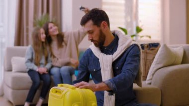 Kameraya bakan ciddi bir adam arka planda seyahat çantasına giysiler koyar anne ve kızı sınıfta selfie çeker. Mutlu ol. Turizm çifti macera yaşam tarzı. Yavaş çekim