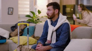 Portre üzgün adam, arka planda seyahat çantasıyla koltukta oturan kameraya bak. Anne ve kızı eğleniyorlar. Sınıfa kıyafet atıyorlar. Turizm çifti macera yaşam tarzı. Yavaş çekim