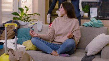 Gergin genç bayan meditasyon egzersizleri yapmaya çalışıyor. Arka planda baba-kız eğlenirken sınıfa kıyafet atıyorlar. Turizm. Dağınık. Yavaş çekim