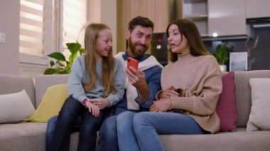 Sosyal medya uygulamasında akıllı telefonlara bakan genç bir aile evdeki kanepede oturuyor. Gadget aşk eğlencesi akıllı telefon kutlaması. Yavaş çekim