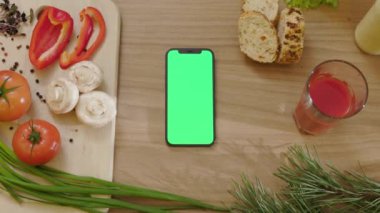 Mutfak telefonunda dikey yeşil ekranda sebzelerin etrafındaki ahşap tablette. Sağlıklı yemek. Vejetaryen blog yazarı. Yavaş çekim
