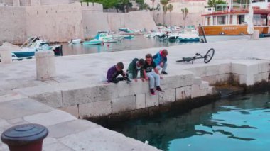 Gün batımında deniz kanalı ve eski kasabanın yakınında oturan bir grup çocuk. Mimari Akdeniz tarihi okyanusu. Çocuklar işte. Kapatın. Yavaş çekim