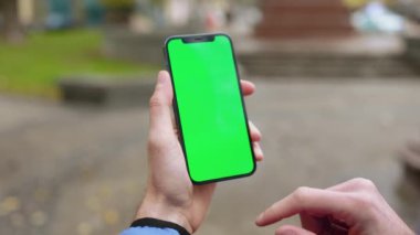 Sokakta dikey yeşil ekranlı cep telefonu tutan bir adam. Akıllı telefon teknolojisi cep telefonu dokunmatik mesaj görüntüsü. Yavaş çekim