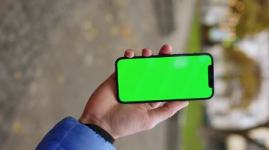 Sokakta yeşil ekranlı cep telefonu tutan dikey bir adamın fotoğrafı. Akıllı telefon teknolojisi cep telefonu dokunmatik mesaj görüntüsü. Yavaş çekim