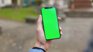 Cadde üzerinde dikey yeşil ekranlı cep telefonu tutan bir adamın fotoğrafı. Akıllı telefon teknolojisi cep telefonu dokunmatik mesaj görüntüsü. Yavaş çekim