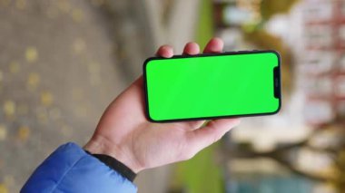 Sokakta yeşil ekranlı cep telefonu tutan dikey nişancı. Akıllı telefon teknolojisi cep telefonu dokunmatik mesaj görüntüsü. Yavaş çekim