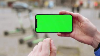 Elinde yeşil ekran arka plan elektrikli scooterlı bir cep telefonu olan dikey çekim yapan bir adam. Akıllı telefon teknolojisi cep telefonu dokunmatik mesaj görüntüsü. Yavaş çekim
