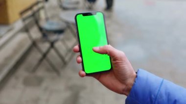 Sokakta çalışan bir adam dikey yeşil ekran arka plan terası olan bir telefon kullanıyor. Açık havada internet krom bulanıklığı var. Cep telefonu medya aygıtı. Yavaş çekim