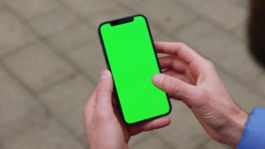Elinde akıllı bir telefonla arka sokaktaki dikey yeşil ekranlı telefona dokunan genç bir adam. Mesaj işi erkek sokak aletleri dijital ekipman interneti. Yavaş çekim