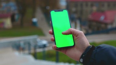 Dikey yeşil ekran arka plan sokak şehirli telefon kullanan eller görüntüsü insanları bulanıklaştırdı. Açık havada internet krom. Cep telefonu medya aygıtı modern hücresel. Yavaş çekim