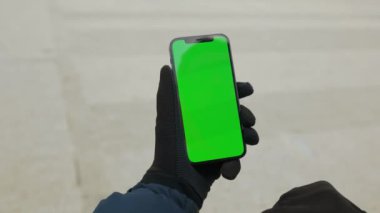 Eldivenli, elinde yeşil ekran akıllı telefonlu bir adam arka planda gri olarak kalıyor. Uygulama bilgileri mobil internet aygıtı. Yavaş çekim