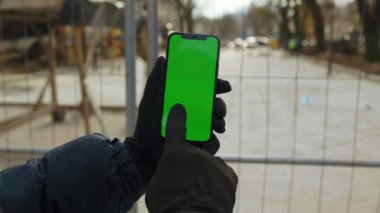Elleri eldivenli, elinde yeşil ekranlı akıllı telefonlu bir adam sokakta oturuyor. Uygulama bilgileri mobil internet aygıtı. Yavaş çekim