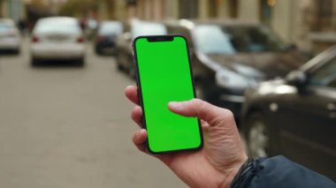 Elinde manken tutan genç adam sokakta dikey yeşil ekranlı telefona dokunuyor ve çalıyor. Sosyal ağlar. Açık havada. Uygulama cep telefonu. Yavaş çekim
