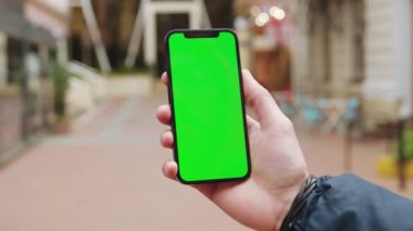Sokakta çalışan bir adam dikey yeşil ekran arka plan terası olan bir telefon kullanıyor. Açık havada internet krom bulanıklığı var. Cep telefonu medya aygıtı. Yavaş çekim