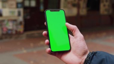 Sokak Terace City 'de dikey yeşil ekran arka planlı telefon kullanan kapalı eller açık havada internet krom bulanık. Cep telefonu medya aygıtı. Yavaş çekim