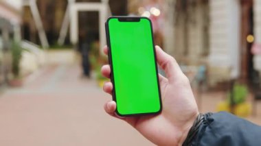 NEW YORK - 19 Aralık 2020: Dikey yeşil ekran arka plan terası olan telefonu kullanan eller açık havada internet krom bulanıklaştırdı. Cep telefonu medya aygıtı. Yavaş çekim