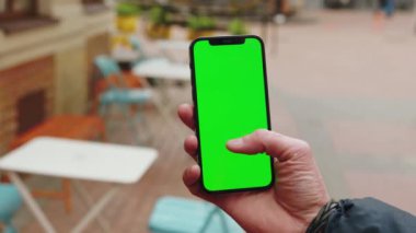 NEW YORK - 19 Aralık 2020: Yavaş çekim adamı dikey yeşil ekran arka plan terası olan telefonu kullanarak açık havada internet krom bulanıklaştırdı. Cep telefonu medya aygıtı. Kapat.