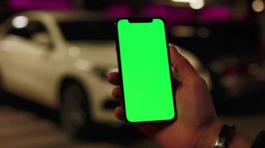 Kapatın elleri adamım. Telefonu tutun. Dikey yeşil ekran arka planı olan beyaz bir araba yolda. Gece lambalarında, şehir sokak akıllı telefonları dokunmatik ekranda. Yavaş çekim