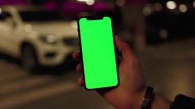 Eller yukarı, telefon kullanın. Dikey yeşil ekran arka plan beyaz araba yolda. Gece lambalarında, şehir sokak akıllı telefonları dokunmatik ekranda. Yavaş çekim