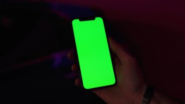 Karanlık ellerde erkek, gece lambasında pembe arka planda dikey yeşil ekranlı telefon kullanır. İyi akşamlar akıllı telefon ekran uygulaması. Teknoloji dokunmatik hücre ekranı. Yavaş çekim