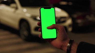 Elle çekilen görüntüler, adamım, telefon kullan. Dikey yeşil ekran arka planda beyaz araba kullan. Gece lambalarında, şehir sokak akıllı telefonları dokunmatik ekranda. Yavaş çekim