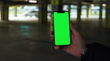 Elinde dikey cep telefonu olan, yeşil ekran arka planda boş park yeri olan bir adamın fotoğrafı. Akıllı telefon teknolojisi şehrin dokunmatik arka planında. Yavaş çekim