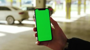 Kapatın elleri adamım. Telefonu tutun. Dikey yeşil ekran arka planı olan beyaz arabaları güneş ışığı parkında tutun. Şehir sokağı akıllı telefon dokunmatik ekranı. Yavaş çekim