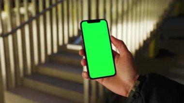 Arkadaki merdivenlerde dikey yeşil ekranla genç elleri tutan ve telefona dokunan adamı kapatın. Akıllı telefon dokunmatik dokunmatik dokunmatik interneti göster. Yavaş çekim