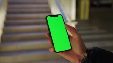 Arkadaki merdivenlerde dikey yeşil ekranla adamın el ele tutuşup telefona dokunuşu. Akıllı telefon dokunmatik dokunmatik dokunmatik interneti göster. Yavaş çekim