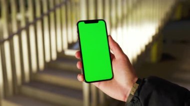 Arkadaki merdivenlerde dikey yeşil ekranlı telefonu tutan ve dokunan genç eller. Akıllı telefon dokunmatik dokunmatik dokunmatik interneti göster. Yavaş çekim
