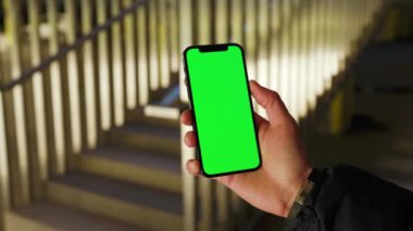 Erkek el ele tutuşup arka merdivenlerde dikey yeşil ekranla telefona dokunuyor. Akıllı telefon dokunmatik dokunmatik dokunmatik interneti göster. Yavaş çekim