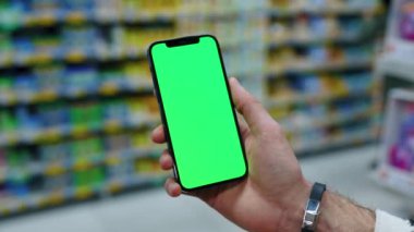 El kullanımı cep telefonu. Arka planda bulanık süpermarkette dikey yeşil ekran var. Model dinleme görüntülü kromakey telefon. Yavaş çekim