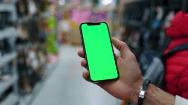 Süpermarkette dikey yeşil ekranlı el kullanımlı akıllı telefon insanları bulanıklaştırdı. Model dinleme görüntülü kromakey telefon. Yavaş çekim