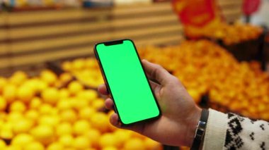 El çekimi, arka planda bulanık meyveler içeren dikey yeşil ekranlı cep telefonu kullan. Limon ve orangutan. Model dinleme görüntülü kromakey telefon. Yavaş çekim