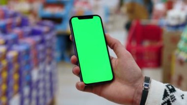 Eller süper markette dikey yeşil ekran ürünü bulanık arka planda cep telefonu kullanır. Model dinleme görüntülü kromakey telefon. Yavaş çekim